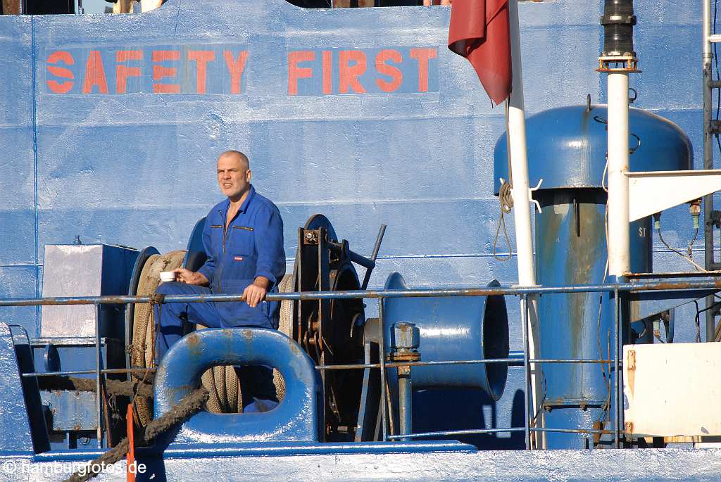 id113210 Matrose mit Kaffeetasse an der blauen Boardwand steht in roten Buchstaben SAFETY FIRST