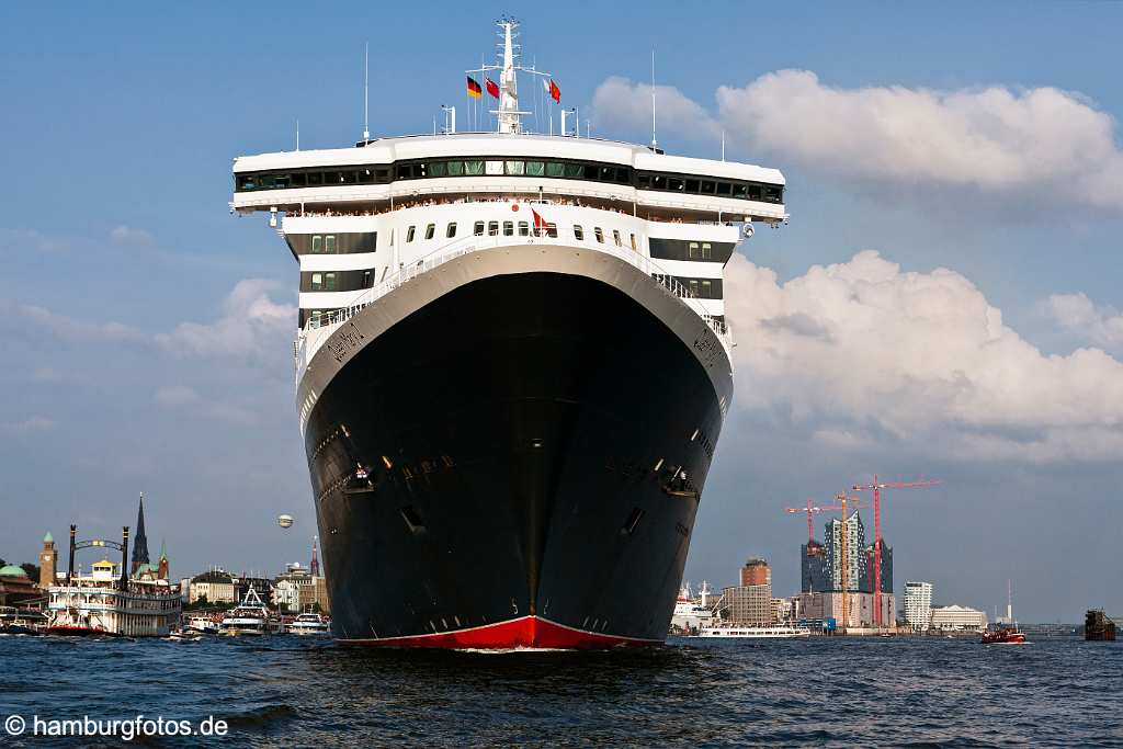 bz0414 Das Kreuzfahrtschiff "Queen Mary 2" laeuft aus dem Hamburger Hafen aus, zahlreiche kleine Schiffe begleiten den Luxusliner. An Deck stehen winkende Passagiere. Im Hintergrund die Baustelle der Elbphilharmonie und die Hamburger Landungsbruecken, sonnig