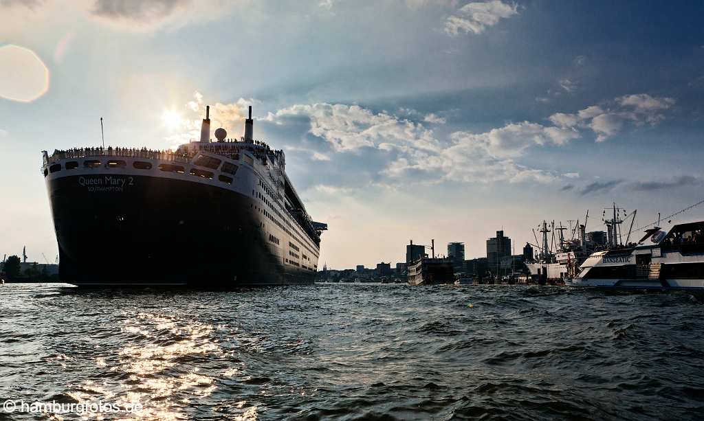 bz0451 Das Kreuzfahrtschiff Queen Mary 2 laeuft aus dem Hamburger Hafen aus. Zahlreiche Passagiere stehen an Deck. Gegenlicht, Abendstimmung