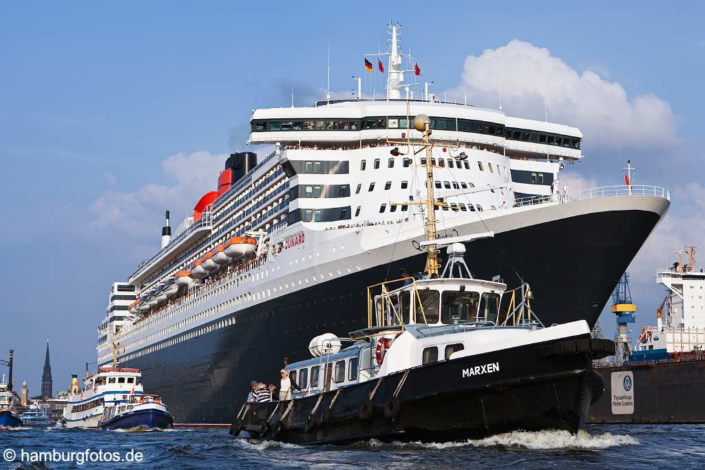 bz0473 Das Kreuzfahrtschiff "Queen Mary 2" laeuft aus dem Hamburger Hafen aus, zahlreiche kleinere Schiffe begleiten den Luxusline ein STueck auf seiner Reise. An Deck stehen winkende Passagiere, sonnig. Im Hintergrund der Pegelturm der Landungsbruecken und die Nikolaikirche