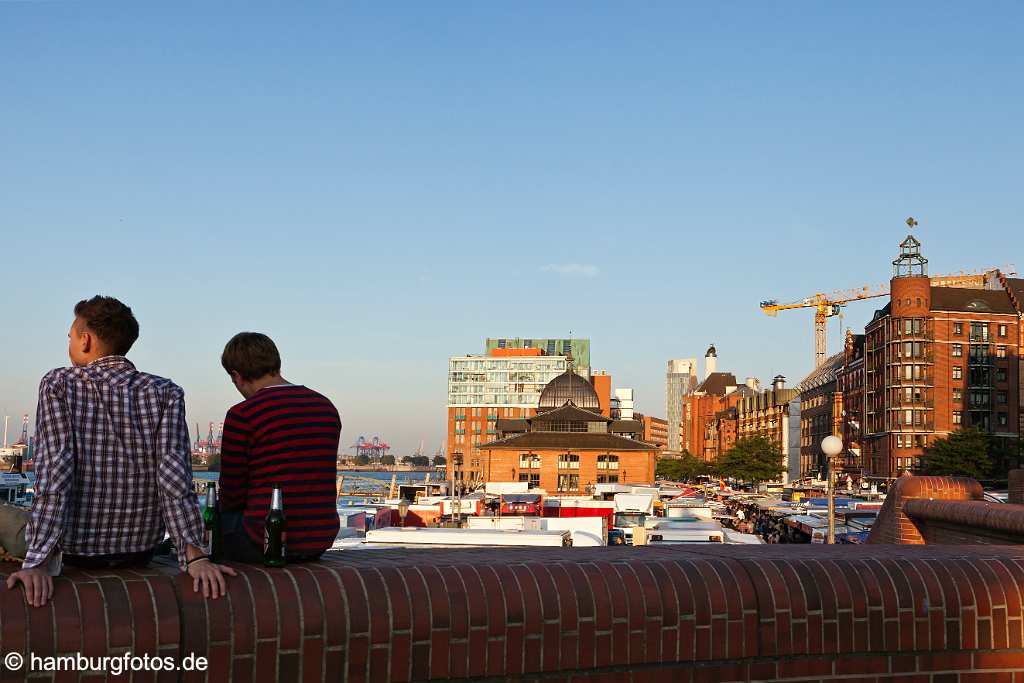 bz0533 zwei junge Maenner sitzen auf der Hafenmauer und geniessen den Blick ueber den Hamburger Fischmarkt und die Elbe an einem sonnigen Sommermorgen