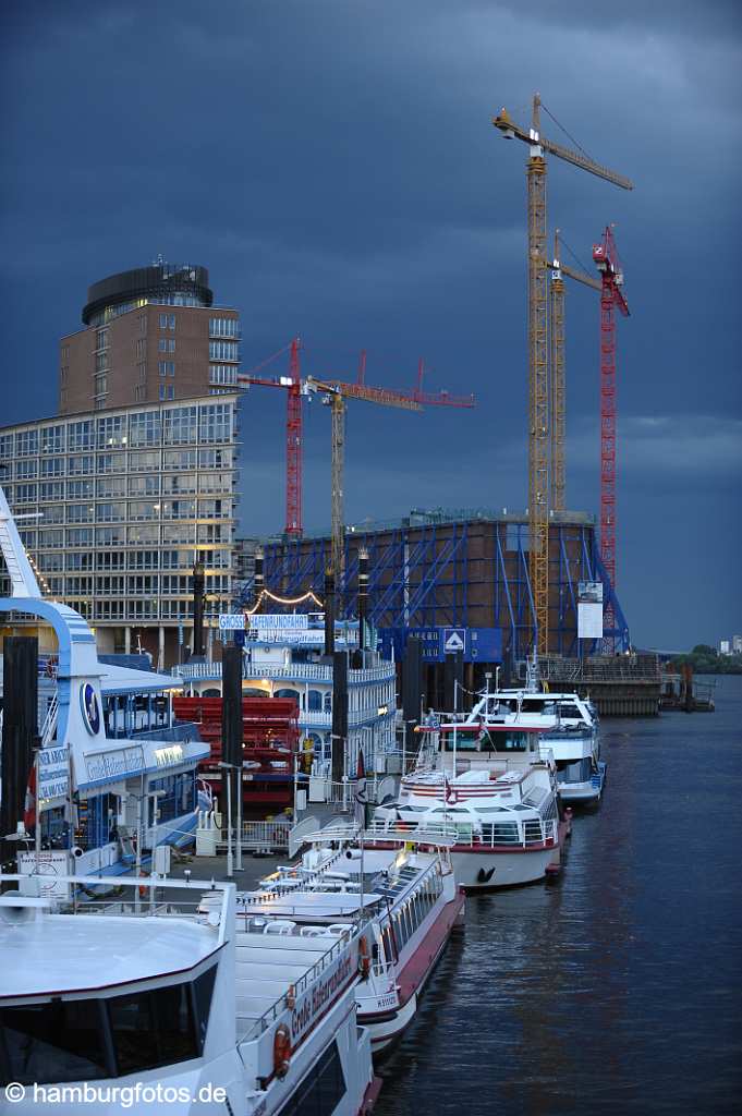 id501076 Hamburg bei Nacht, HTC- Hanseatic Trade Center auf der Kehrwiederspitze, dahinter die Baustelle der Elbphilharmonie mit Kranen und im Vordergrund diverse Ausflugsschiffe.