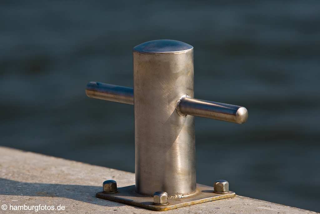 id114293 Edelstahl-Poller am Kai eines Yachthafens schimmert in der Sonne, Hintergrund Wasser