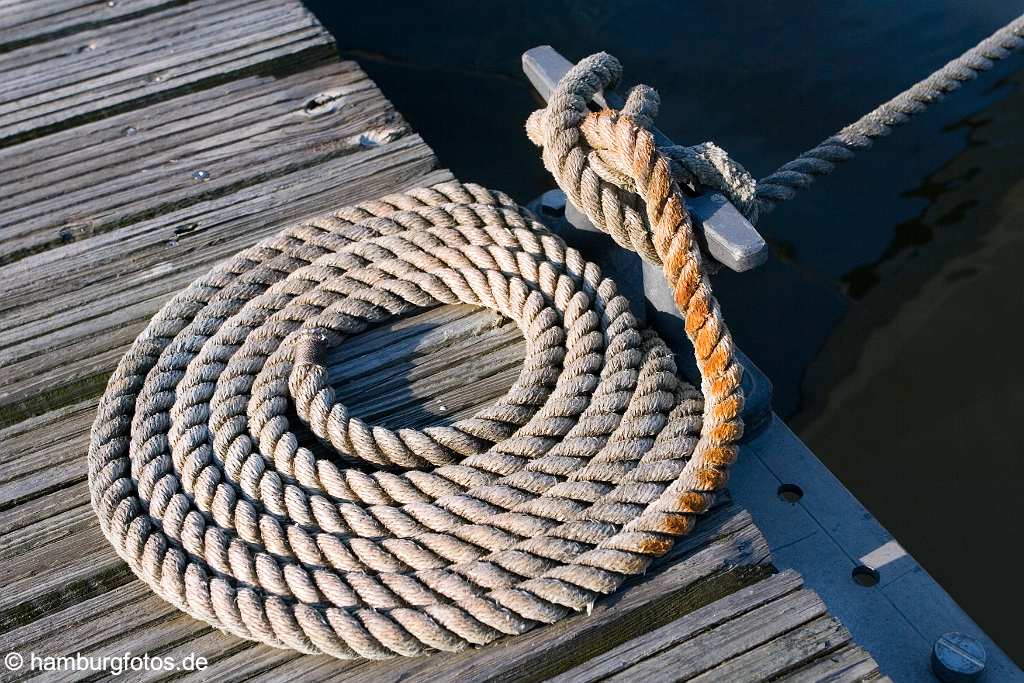 id114369 Tampen liegt ordentlich zu einer Schnecke zusammengerollt auf einer Mole. Ein Ende is mit einem Poller verknotet und haelt ein Schiff an seinem Hafen-Liegeplatz fest